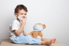 教你的孩子预防病毒和流感的措施。宝贝，戴着医疗面具的男孩把医疗面具戴在他的玩具熊玩具上。照顾所爱的人。基本卫生规则