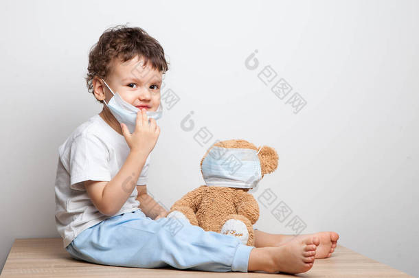 教你的孩子预防病毒和流感的<strong>措施</strong>。宝贝，戴着医疗面具的男孩把医疗面具戴在他的玩具熊玩具上。照顾所爱的人。基本卫生规则
