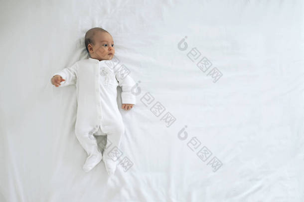 新生儿躺在白色的背景上. 一个穿白衣的小孩正朝镜框看去.