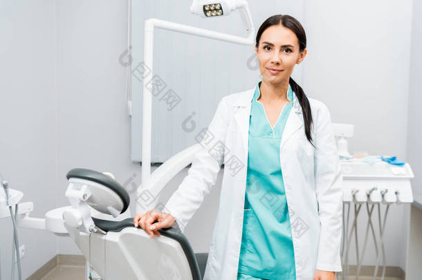 有吸引力的牙医站在椅子附近的牙科诊所