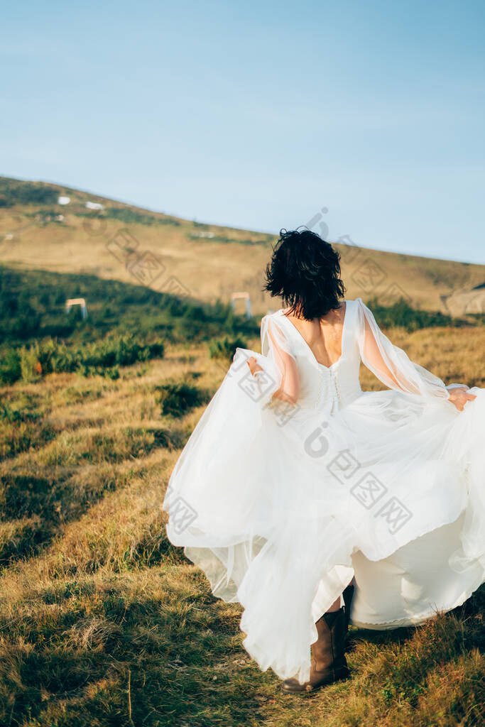 穿着婚纱的女人的后视镜正待在高山上，强烈的秋风