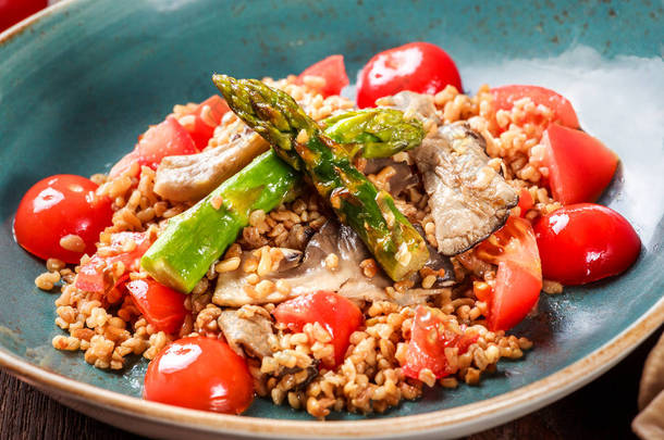 健康的大麦粥配芦笋, 西红柿和蘑菇在盘子里。素食食品