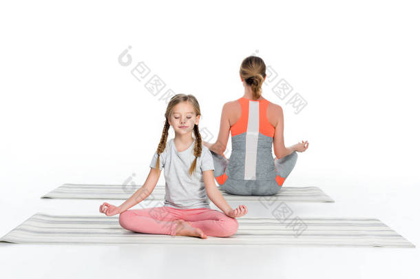 运动的母亲和女儿练习瑜伽垫一起隔离在白色