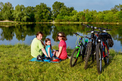 家庭自行车骑在户外，活动的父母和孩子骑自行车和放松附近美丽的河