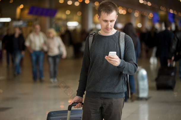 年轻的旅行者在机场中使用手机 