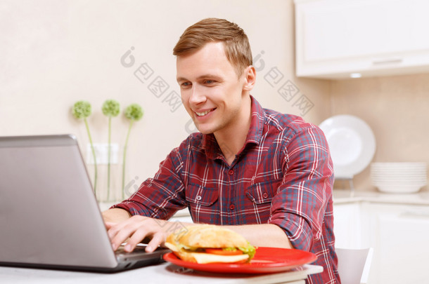 在厨房里的计算机上工作的男人微笑着