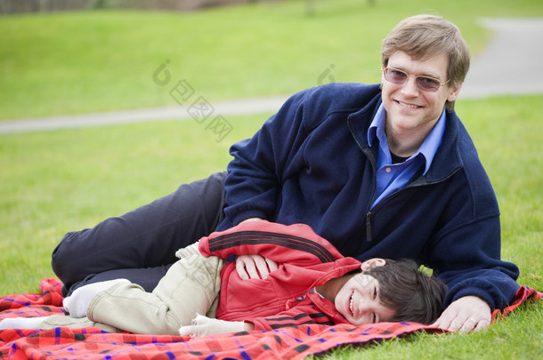父亲躺在毯子上，儿子在公园