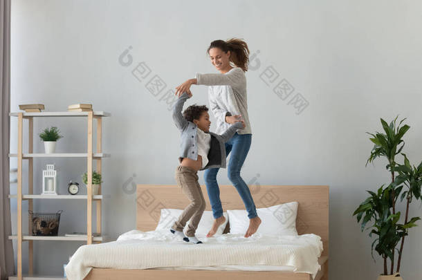 快乐的妈妈和可爱的笑着的小儿子在床上跳舞.