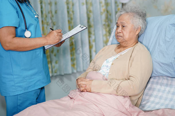 医生在护理医院病房的<strong>病床</strong>上与亚洲老年或老年老太太谈论诊断和笔记：健康强医疗理念