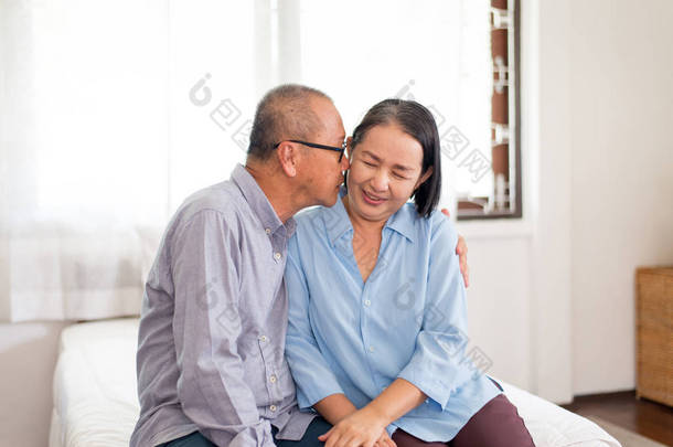 在家里，一对快乐的老亚洲情侣在床上亲吻着<strong>脸蛋</strong>