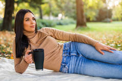 秋天，美丽的女人在公园边喝咖啡边欣赏.