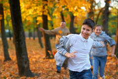 快乐的家庭在秋天的城市公园里度假. 孩子和父母跑步，微笑，玩耍，玩乐。 明亮的黄树和树叶