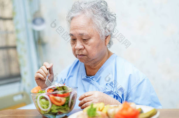 亚洲<strong>老人</strong>或老年老太太妇女病人吃早餐健康的食物与希望和快乐, 而坐在病床上, 饿在<strong>医院</strong>