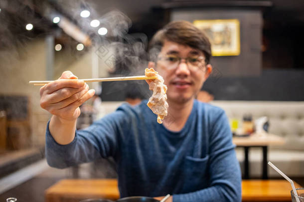 在日本的Shabu餐馆里，男人拿着<strong>竹签</strong>和一片煮熟的牛肉
