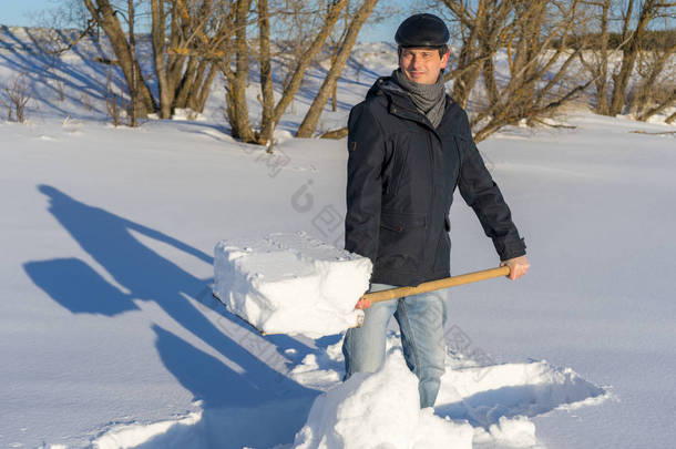 在阳光明媚的日子里，英俊的中年男子在自家的地块上清扫雪地。 人与铲子铺路从乡村房屋到道路。 冬季主动休闲活动概念