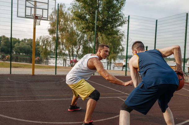 两名篮球运动员在室外场地打激烈的比赛. 男子运动员穿着运动服在街头篮球训练中比赛