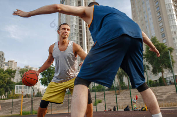 两名球员在篮球场中心的室外场地上. 男子运动员穿着运动服在街头篮球训练中比赛
