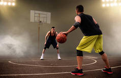 两个篮球运动员制定了战术，黑暗的背景。 男子运动员穿着运动服在街头篮球训练中比赛
