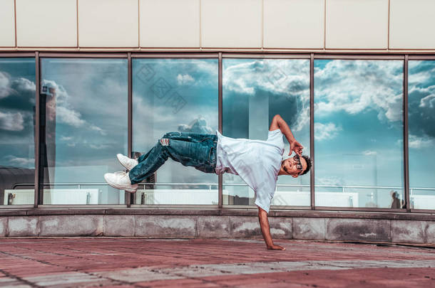 男子运动员男子舞蹈家。 背景玻璃窗云。 一只手飞起来. 时尚的霹雳舞风格,健身运动嘻哈. 都市文化，街头舞蹈。 杂技表演.