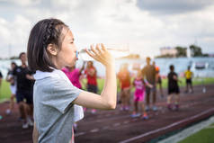 亚洲女孩拿着一瓶水，在阳光下从塑料瓶喝水的肖像，女运动员在跑步后休息，喝水，以弥补汗水损失，减少在炎热的晴天口渴 
