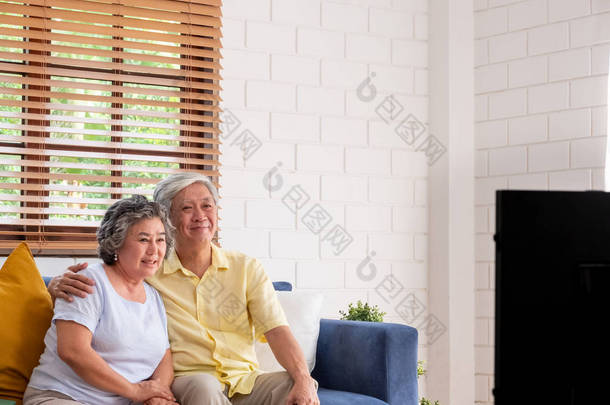 亚洲夫妇高级坐在坐在一起，在生活里看电视