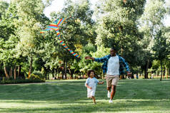 快乐的非洲裔美国人的孩子运行与父亲和风筝在公园