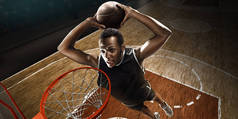 身着运动服的非洲裔美国篮球运动员在职业篮球场上带球。扣篮。从箍的高角度视图