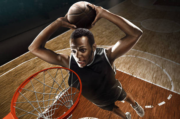 身着运动服的非洲裔美国篮球运动员在职业篮球场上带球。扣篮。从箍的高角度视图