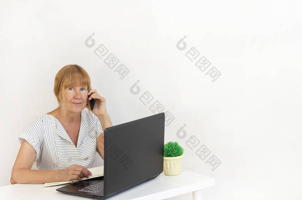 使用笔记本电脑的高级妇女。女商人在办公室用笔记本电脑工作。女商人打电话，并采取了。复制空间。您的文本
