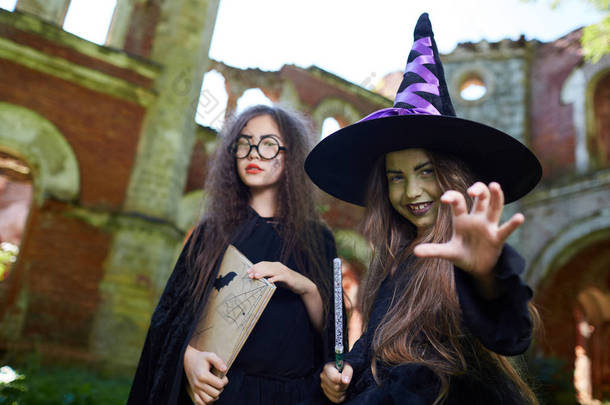 腰起两个十几岁的女巫看着相机，而在万圣节在怪异的城堡摆姿势，复制空间
