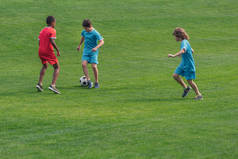 可爱的多元文化男孩在运动服上踢足球在草地上 
