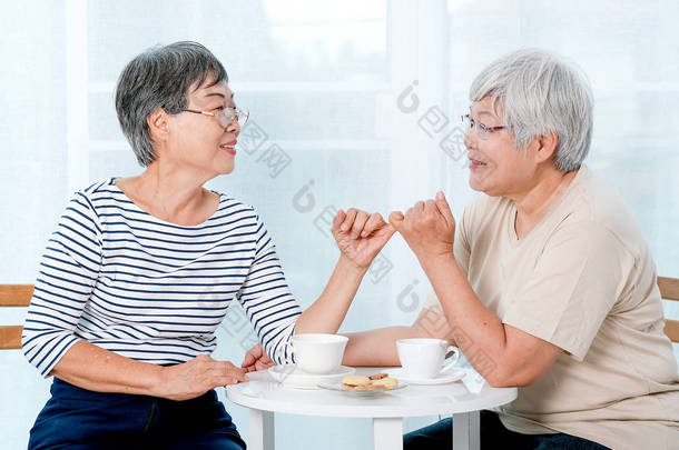 两位亚洲老年妇女在房子的阳台前互相钩住小手指，面带微笑.