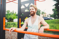 肖像年轻的胡子男子站在公共运动场上和平行酒吧训练。英俊的锻炼运动员。肖像运动男子与胡子，训练后休息。户外夏季锻炼