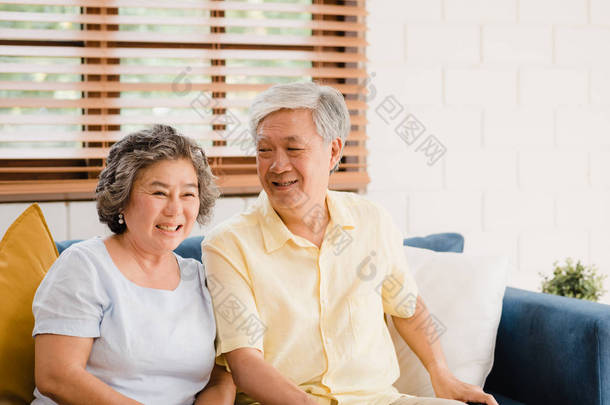 在家里客厅里看电视的一对亚洲老夫妻，在家里放松的时候，躺在沙发上享受爱情的时刻。享受家庭幸福的生活方式.