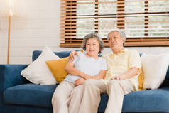 在家里客厅里看电视的一对亚洲老夫妻，在家里放松的时候，躺在沙发上享受爱情的时刻。享受家庭幸福的生活方式.