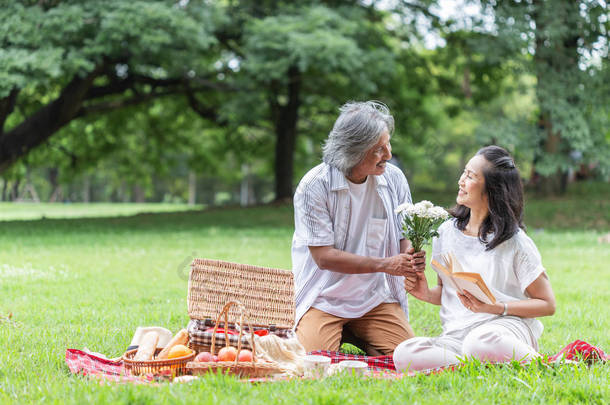 亚洲老年夫妇野餐，并给花与爱在花园