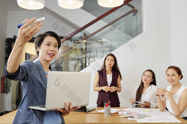 亚洲年轻商务培训师手里拿着笔记本电脑,在商务培训期间向女商人<strong>讲解</strong>新的商业方式
