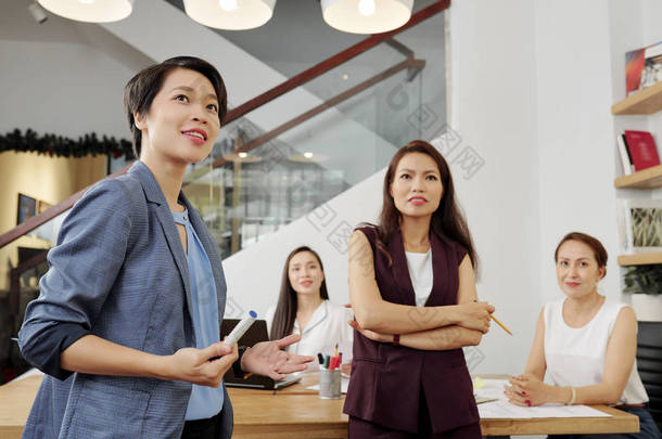 年轻的亚洲女商人在办公室商务研讨会期间站在团队中工作