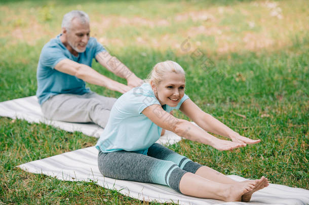 微笑成熟的男人和女人练习瑜伽姿势，而坐在瑜伽垫