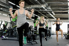 运动，健美，生活方式和人的概念 - 年轻男子和两个女人与杠铃弯曲肌肉，使肩膀压蹲在健身房