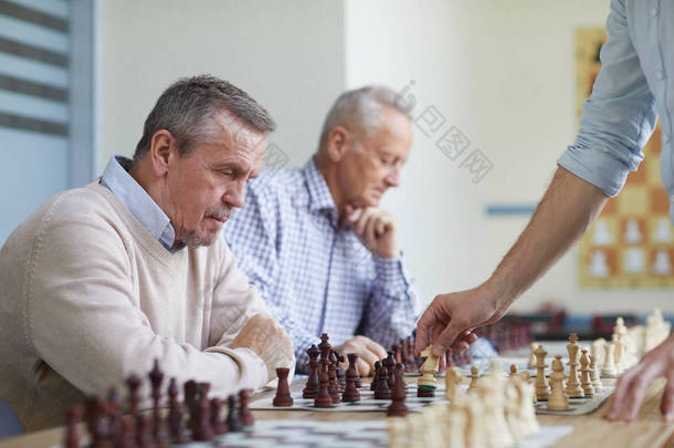 两位银发老人在国际象棋俱乐部与本地特级大师下棋，共度<strong>闲暇时光</strong>