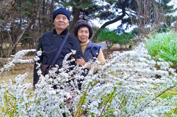 一对年迈的亚洲夫妇在日本花圃旅行时微笑着。退休生活方式概念