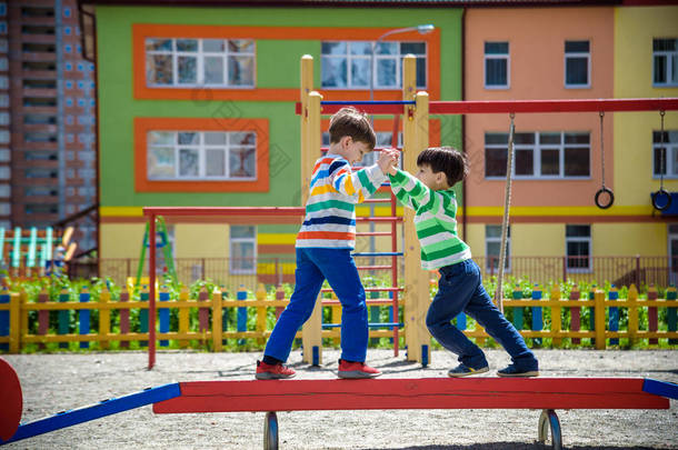 <strong>两个</strong>小学校和学龄前男孩一起在户外操场上玩耍。在阳光明媚的夏日，<strong>孩子</strong>们站在户外活动的圆木上竞争