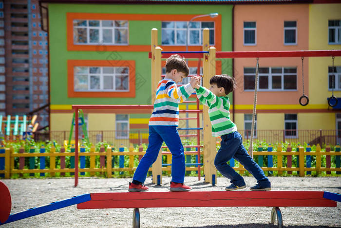 两个小学校和学龄前男孩一起在户外操场上玩耍。在阳光明媚的夏日，孩子们站在户外活动的圆木上竞争