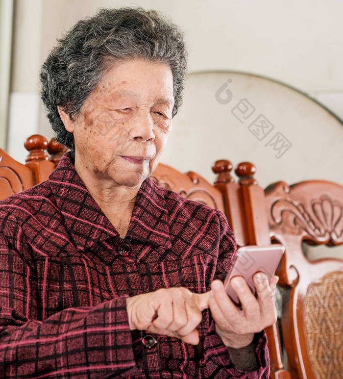 亚洲老妇人坐在现代智能手机上浏览东西，与家里的人建立联系，生活技术，特写