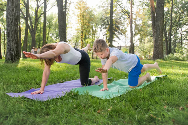 中年母亲与她十几岁的男孩孩子在公园做瑜伽和呼吸练习的照片。家庭在做运动时照顾身心健康