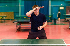 三十岁穿黑色运动服的男子在体育馆打乒乓球。滚在乒乓球的权利
