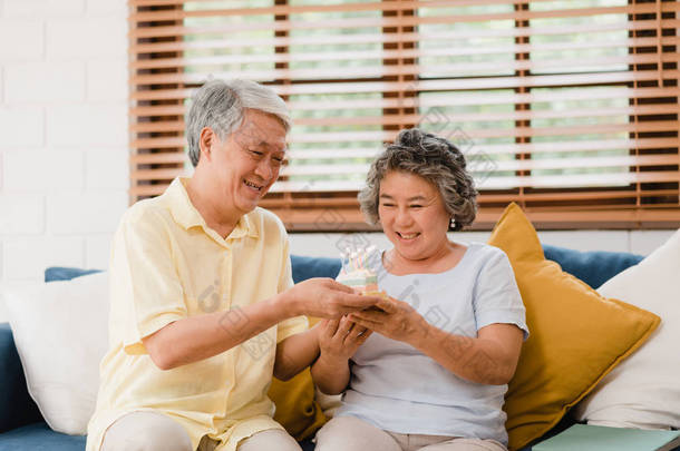 亚洲老年夫妇男子拿着蛋糕<strong>庆祝</strong>妻子的生日在家里的客厅。日本夫妇在家里一起享受爱情时刻。生活方式 老年家庭在家的概念.