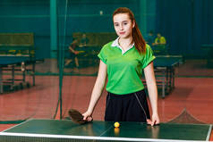 迷人的高加索少女站在乒乓球附近, 看着镜头。年轻的女运动员