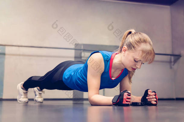 年轻的快乐微笑金发姑娘做木板在健身房。在背景上有许多的粉色和蓝色的运动球.